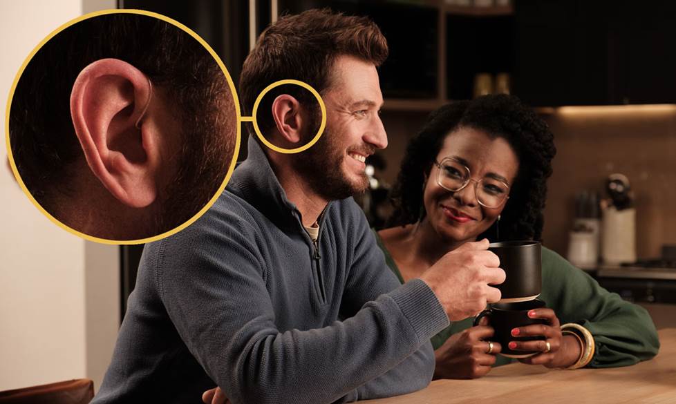 A man sitting at a dinner table with people talking. He is wearing Sennheiser Conversation Clear Plus earbuds.