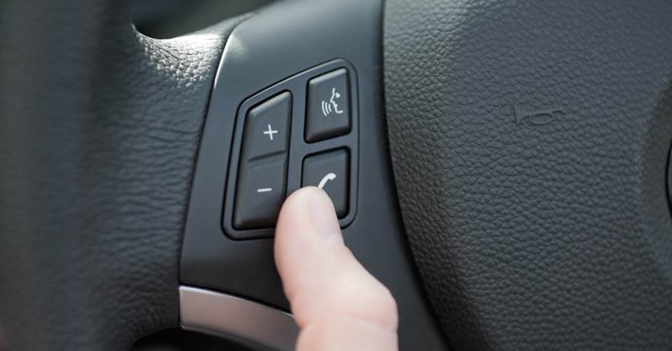 image of a person's thumb pressing a button on the steering wheel to answer a phone call.
