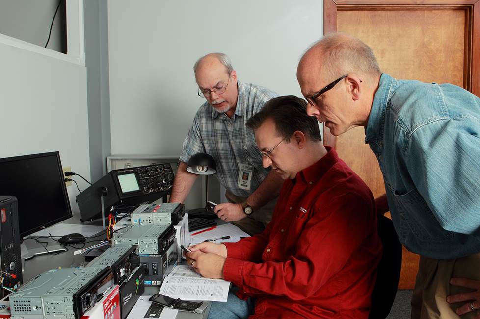 Three men in the Crutchfield labs looking at car stereos.