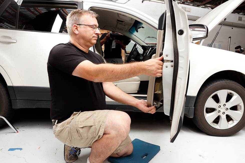 person kneeling on shop floor, pulling panel off of car door