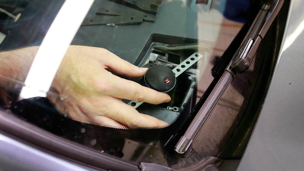 Hand installing a tweeting in dash, viewed through front windshield