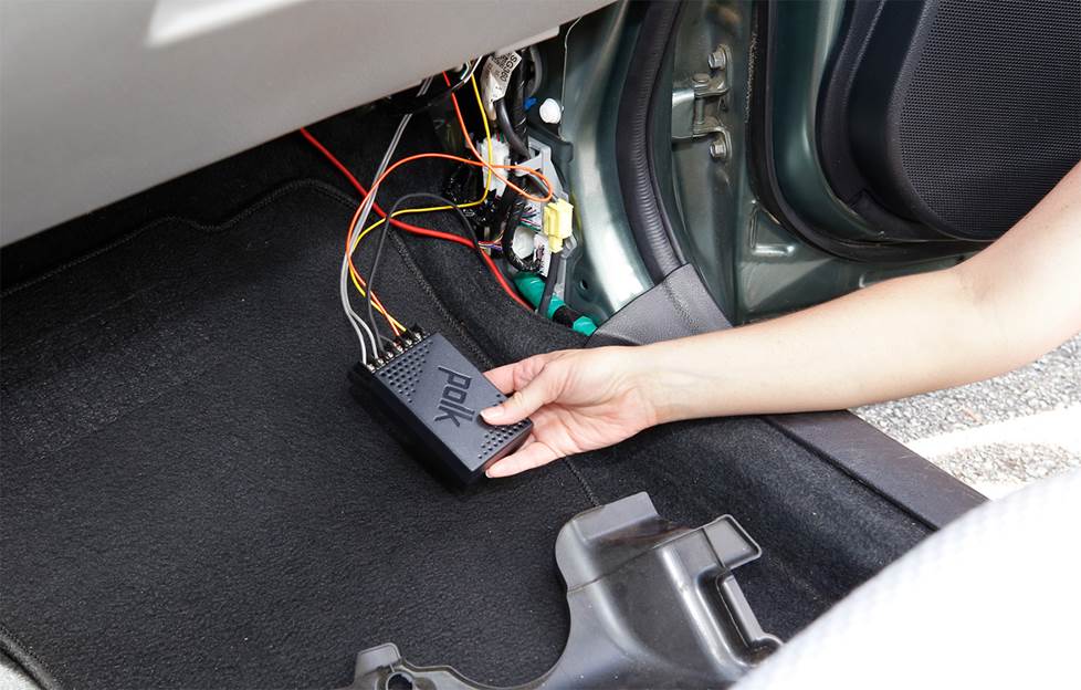 hand placing a speaker crossover behind kick panel
