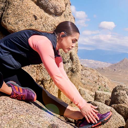 Woman wearing JBL Endurance PEAK true wireless earbuds on mountain climb.