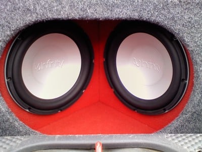Close-up picture of a red and white Infinity subwoofer installed in a box in the car's trunk