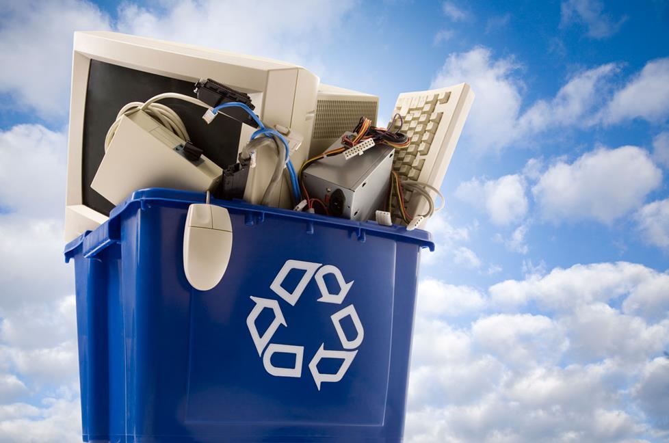 A recycling bin filled with old electronic equipment like a computer, keyboard, and mouse.