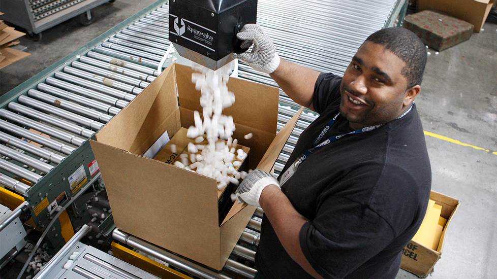 warehouse working fills box with packing peanut from industrial tube