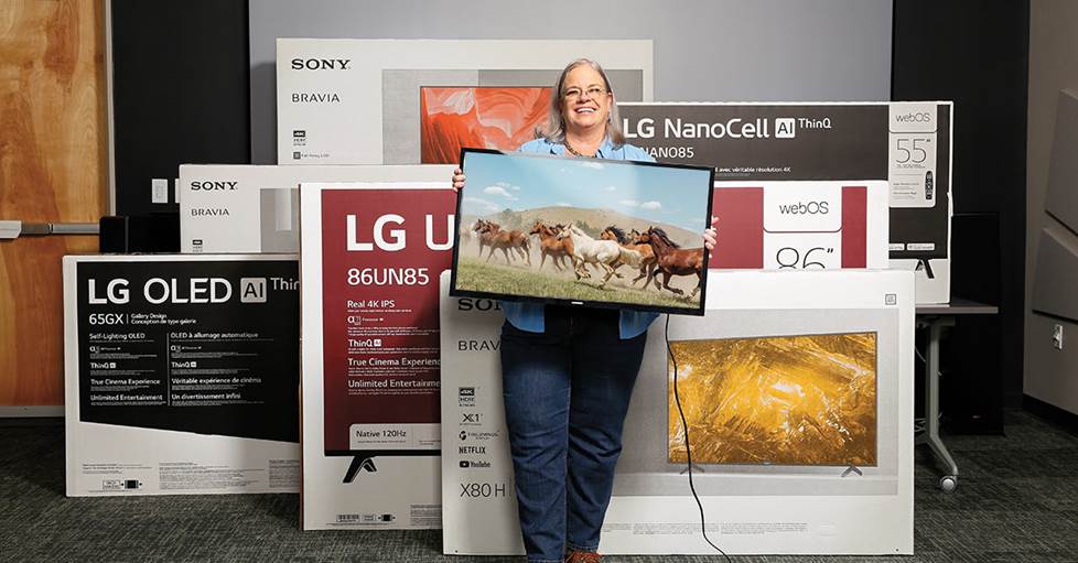 Crutchfield employee surrounded by many tvs of different brands and sizes