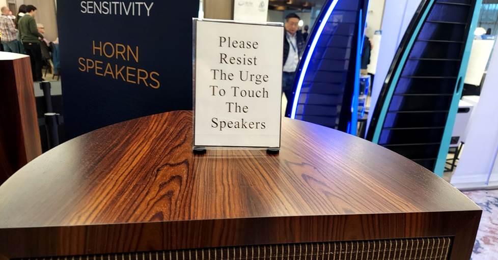 A photo of a sign that reads "Please resist the urge to touch the speakers" sitting on top of a speaker