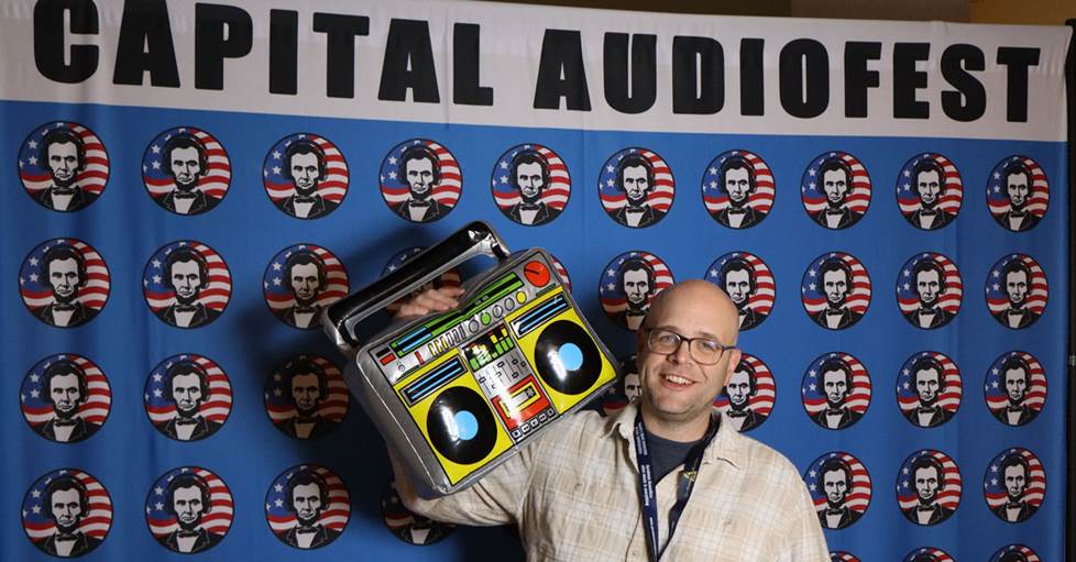 Jeff with an inflatable boombox toy in front of the Capital Audiofest banner